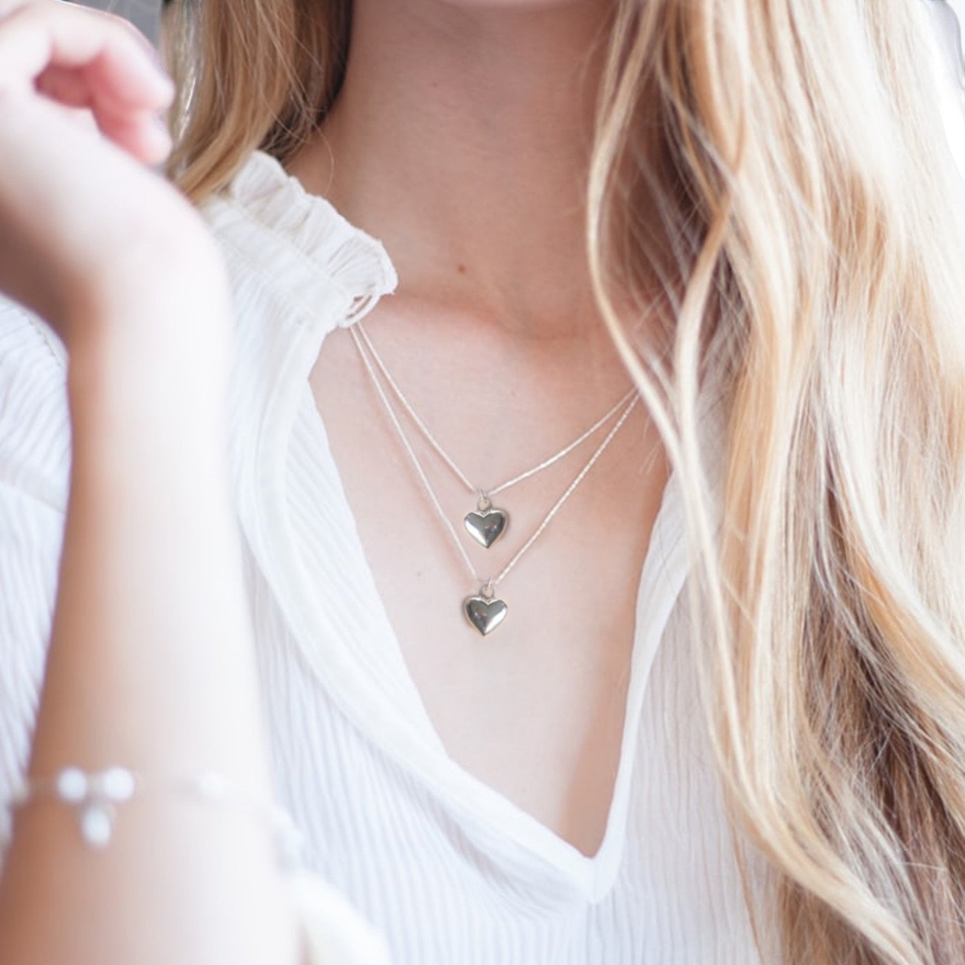 Woman wearing the silver plated puff heart necklace, shown layered with a second chain as a styling idea