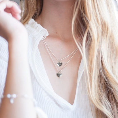 Woman wearing the silver plated puff heart necklace, shown layered with a second chain as a styling idea