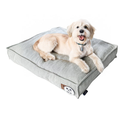 Small white dog lying on the light grey padded dog bed, side view