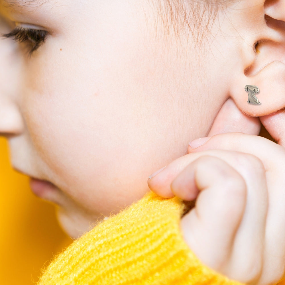 A child wearing one of the puppy dog stud earrings in stainless steel, shown close up on the ear