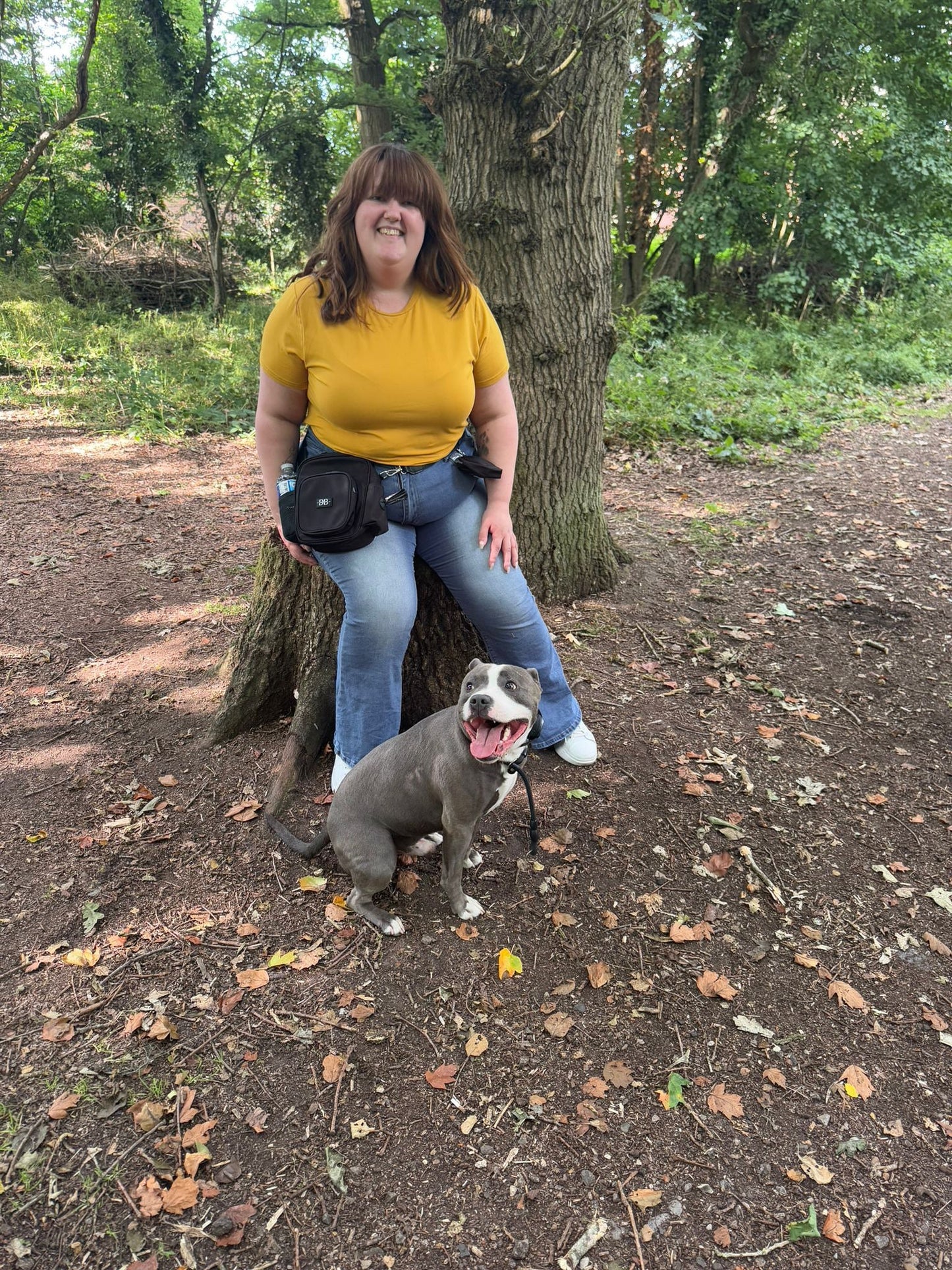 A woman wearing The OG black bag at her waist on a woodland walk with her dog