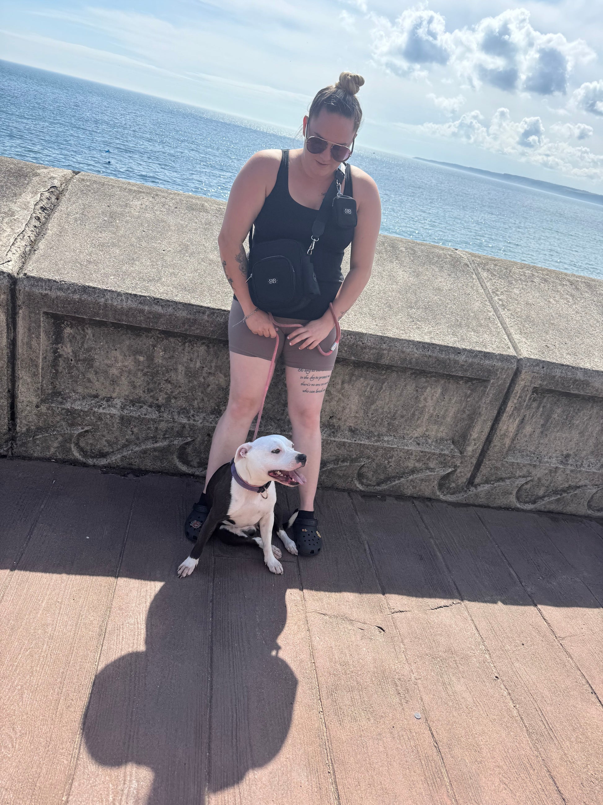 A woman wearing The OG black bag crossbody on a seafront walk with her dog