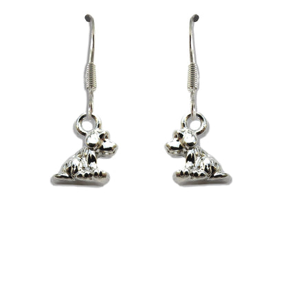 Pair of silver plated little dog drop earrings on fishhook wires, each charm shaped as a seated puppy, on a plain white background.