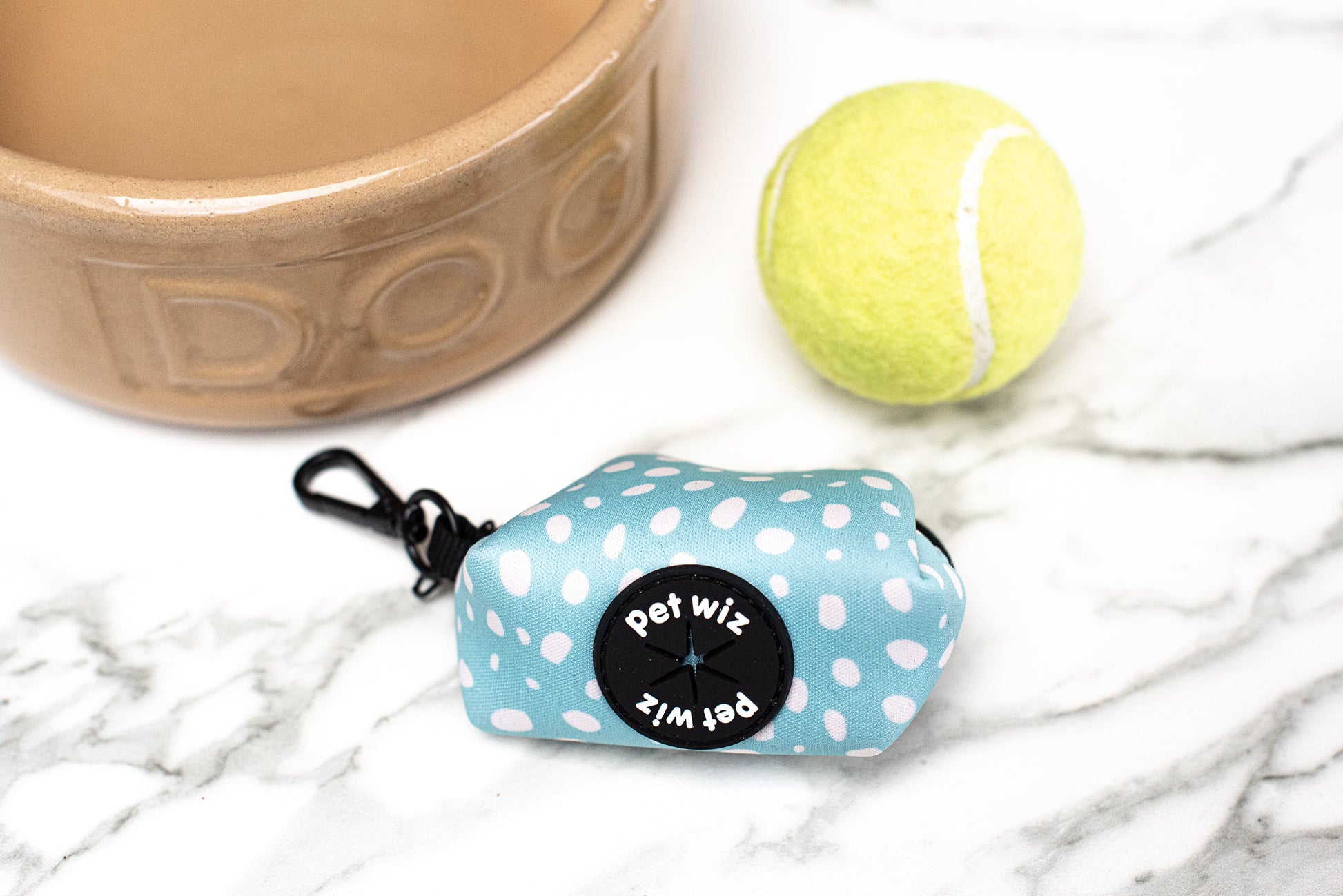 Blue spotted poo bag holder beside a dog bowl and a tennis ball