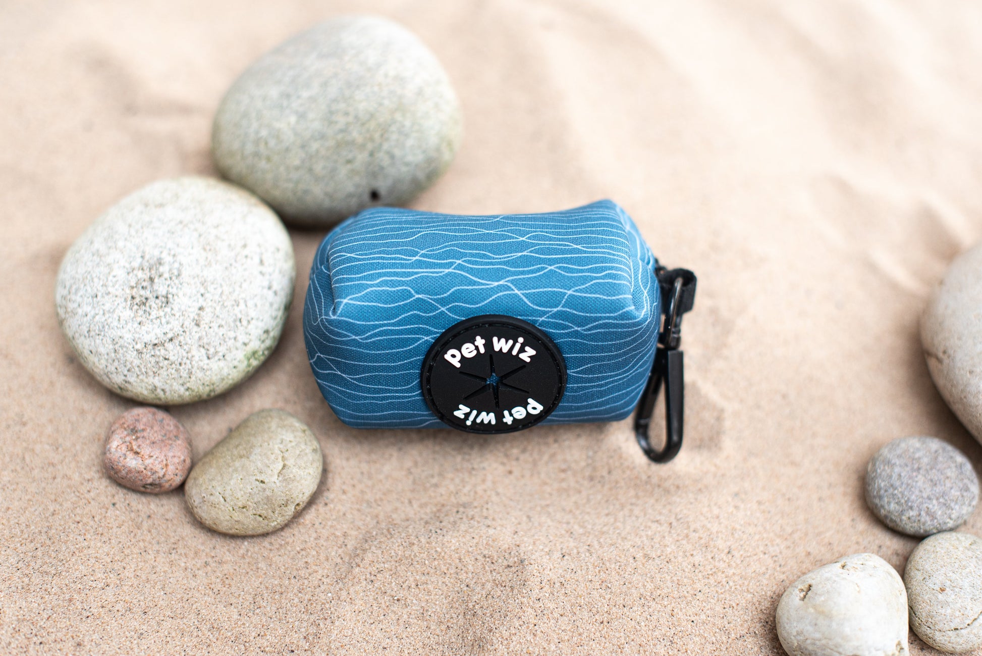 Blue wave pattern poo bag holder with lead clip, photographed on sand